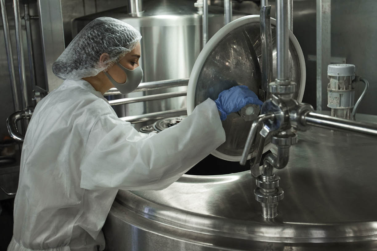 Side view portrait of young female worker operating mixing machine at clean food production factory, copy space