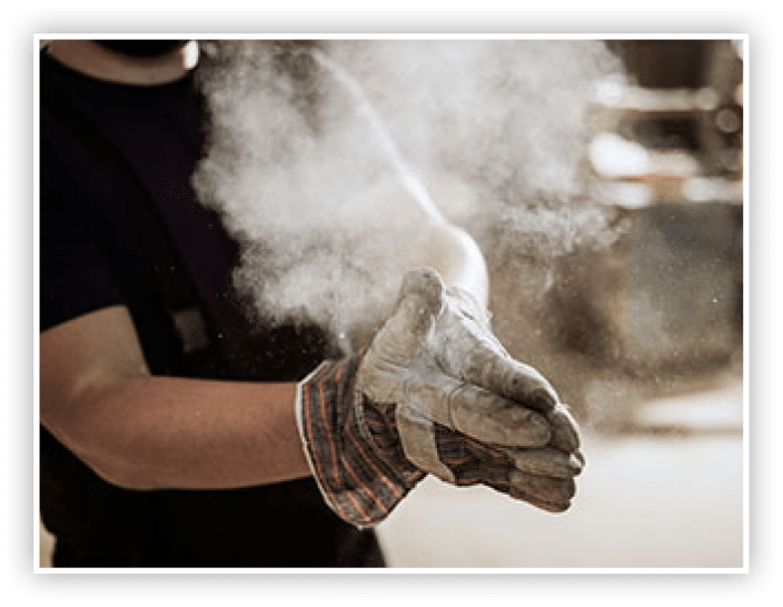 Close up of unrecognizable manual worker cleaning sawdust from his protective gloves in a workshop.